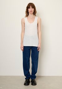 Balta be rankovių marškinėliai su apvaliu iškirpimu, derinami su laisvomis tamsiai mėlynomis džinsais ir juodais beužmaunamais batais.