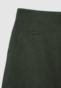 Tessuto in corduroy verde scuro con strisce verticali e una tasca orizzontale con dettagli di cucitura sottili.