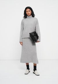 Szürke kötött pulóver magas nyakkal és hosszú ujjakkal, párosítva egy megfelelő bordázott midi szoknyával. Fekete oversized clutch táska és krém színű slip-on cipők.