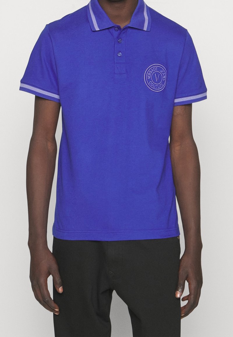 Modrá polo košile vyrobená z měkké tkaniny, se límečkem s kontrastními pruhy a vyšívaným logem na hrudi, krátké rukávy.