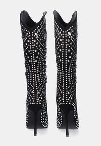 Botas negras hasta la rodilla con un diseño ajustado, cubiertas de tachuelas plateadas, con puntera puntiaguda y tacón alto de aguja. Textura suave.