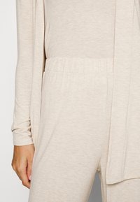 Light beige loungewear set consisting of a long-sleeve top and elastic waistband pants, featuring a soft, textured fabric and relaxed fit.