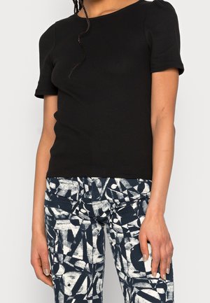 Persoon draagt een strakke zwarte top met korte mouwen en een broek met hoge taille met marineblauwe en witte abstracte geometrische patronen.