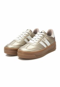 Zapatillas metálicas doradas con rayas blancas, con una parte superior texturizada, cordones blancos y una suela de goma marrón. Diseño de punta redondeada.