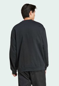 Sort sweatshirt med lange ærmer og ribbede manchetter. Har en rund hals og en blød tekstur. Båret med strukturerede mørke bukser.