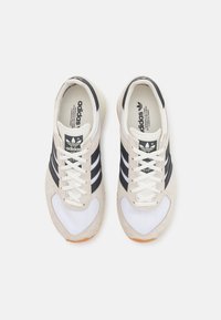 Adidas kedas ar bēšā samta un sieta virsu, melnām svītrām, baltām auklām un gumijas zoli. Caurspīdīgs logs uz mēles.