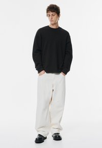 Felpa nera con maniche lunghe e polsini a coste, abbinata a pantaloni bianchi larghi e scarpe chunky nere. Design semplice e minimalista.