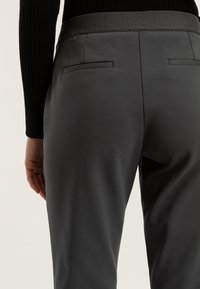 Szare spodnie o gładkiej fakturze, z szerokim paskiem, dwiema tylnymi kieszeniami i dopasowanym krojem.