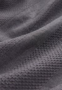 Gray textured fabric showing a woven pattern with a smooth finish and soft drape, highlighting the interplay of light and shadows.