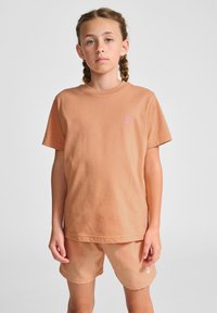  ferskenfarvet bomulds t-shirt med korte ærmer og et lille lyserødt pil-logo. Sættet er kombineret med matchende ferskenfarvede shorts med sidelommer.