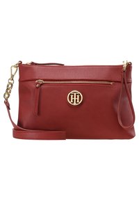 Czerwona skórzana torba na ramię z złotym zamkiem błyskawicznym, odpinanym paskiem, pętlą na nadgarstek oraz okrągłym złotym logo Tommy Hilfiger z przodu.