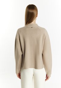 Beige, textuurtrui met een hoge kraag en raglanmouwen. De achterkant heeft een klein logotag boven de halslijn. Zachte, ontspannen pasvorm.