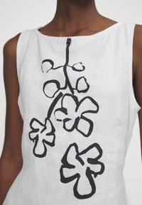 Valkoinen hihaton mekko, jossa on musta kukkaku_viivapiirrosprintti. Kankaassa on hieno rakenne, ja pääntie on pyöreä.