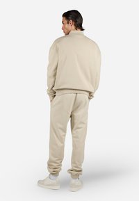 Beige genser og joggebukser i mykt materiale med avslappet passform, ribbede mansjetter og matchende ankeldetaljer. Skoene er lys beige.