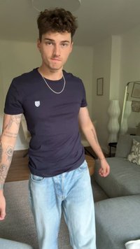 T-shirt navy con piccolo logo sul petto, indossato con jeans azzurri chiari. T-shirt ha una texture liscia; i jeans sembrano avere una vestibilità comoda e risultano leggermente strappati.