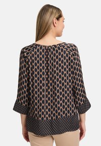 Czarna bluzka z geometrycznym beżowym wzorem, o rękawach do 3/4 i gromadzonym dekoltem. Posiada plisowany tył i warstwowy dół.