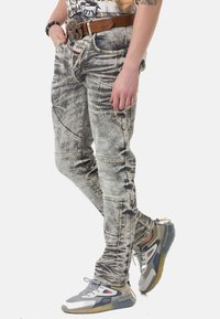Verwaschenes graues Jeans mit einem einzigartigen, abgenutzten Muster, kontrastierenden Nähten, mehreren Taschen und einer klassischen Passform. Kombiniert mit mehrfarbigen Sneakers.