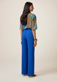 Blue wide-leg trousers in a smooth fabric paired with a patterned short-sleeve blouse featuring blue, brown, and gold tones.