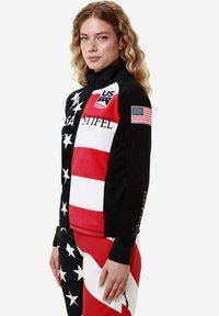 Giacca nera con zip, con sezioni rosse, bianche e blu, caratterizzata da un motivo a stelle e strisce, e il testo "USA" e "STIFEL". Toppa con la bandiera americana.