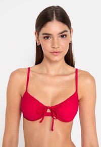 Red bikini top with thin straps, gathered detailing, a front tie closure, and a triangular cup shape. Smooth fabric finish.