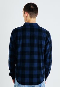 Cămașă din flanel în carouri bleumarin și negru, cu guler cu nasturi și mâneci lungi. Material texturat cu o croială lejeră.