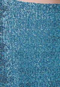 Blå paljett tyg med en glänsande yta, som har en texturerad och reflekterande design. Ljus reflekteras varierande över ytan.