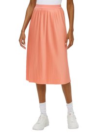 Falda midi plisada en suave tela color durazno, con una pretina alta y un brillo sutil. Combinada con zapatillas blancas y calcetas hasta el tobillo.