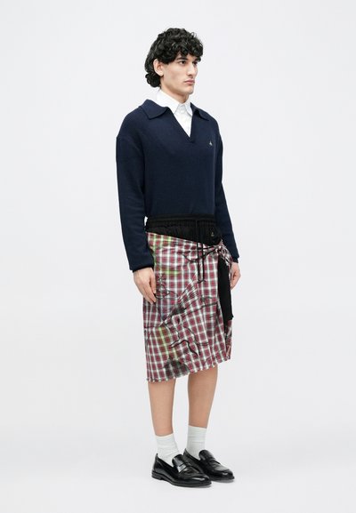 Merevärvikõrge kaelusega kampsun, millele on lisatud punase ja rohelise ruudulise mustriga seelik, millel on must kärbitud vöökoht. Mustad loafersid ja valged sokid.