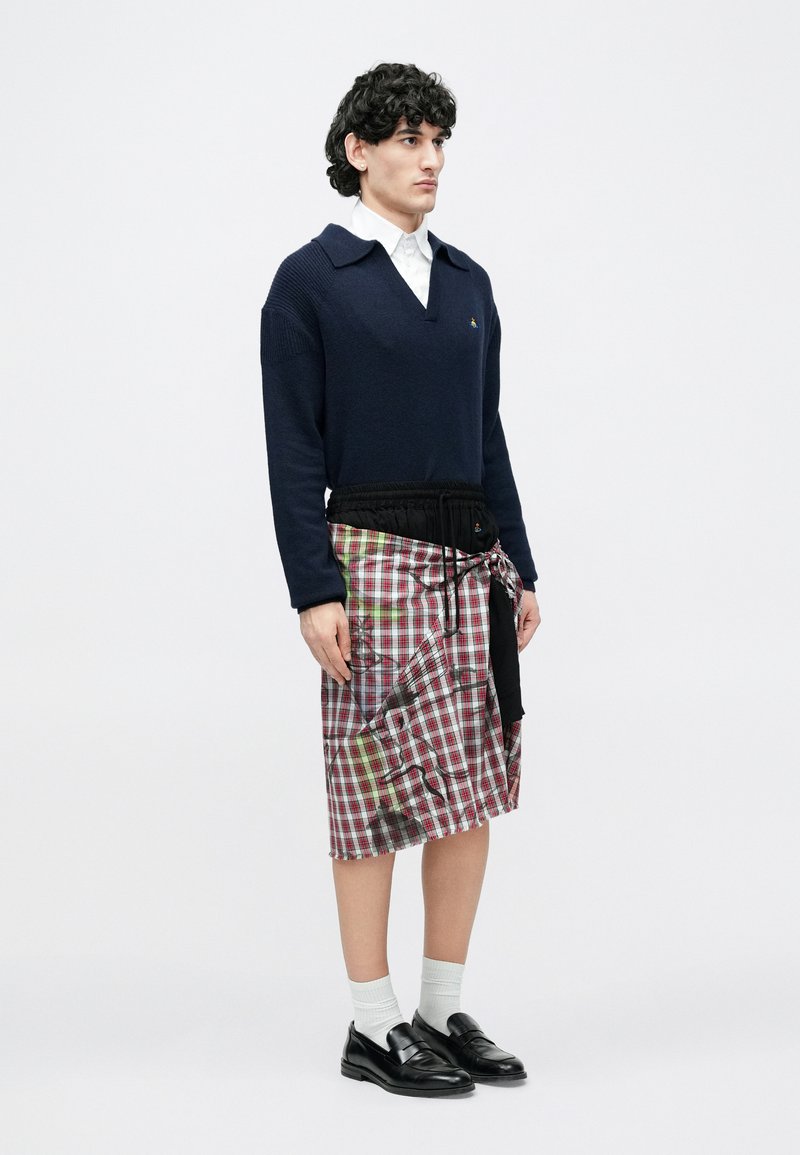 Marineblå sweater med krave, kombineret med et rødt og grønt ternet nederdel med en indsnævret sort taljebånd. Sorte loafers og hvide sokker.