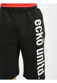 Svarte shorts laget av myk tekstil, med et dristig hvitt vertikalt logotrykk på siden. Behagelig midjebånd med elastisk detalj.