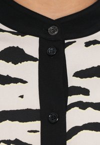 Čierna a krémová blúzka s golierom, zapínaním na gombíky a vzorom tigrej pruhov s žltými akcentmi. Hladká textúra látky.