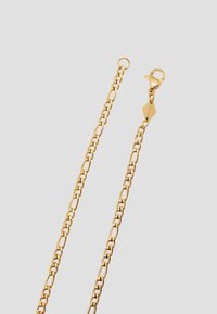 Guldplateret metal kæde med ovale led og en lukning af type lobster, med et lille mærke indgraveret med tekst. Glat overflade og skinnende finish.