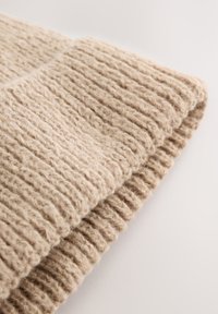 Bonnet beige en tricot réalisé en laine douce. Il présente un motif côtelé texturé et un revers plié pour plus de chaleur et de confort.
