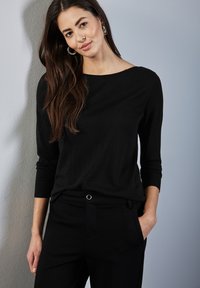 Schwarzes Langarmshirt aus glattem Stoff, mit weitem Ausschnitt und gerippten Bündchen, kombiniert mit gut sitzenden schwarzen Hosen und einer Brusttasche.