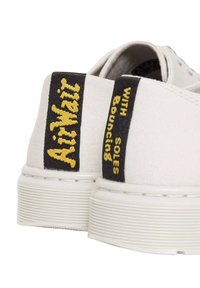 Sneakers bianchi in tela con suole spesse bianche. I talloni neri presentano testo giallo: "AIRWALK" e "WITH SOLES Bouncing." Design semplice.