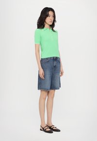 Mint green short-sleeve polo with button detail, paired with mid-length blue denim shorts and black strap sandals, on a neutral background.