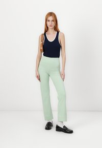 Ναυτικό αμάνικο μπλουζάκι με λευκή ραφή, ανοιχτόχρωμο πράσινο παντελόνι σε χαλαρή γραμμή και μαύρες μπαλαρίνες. Το μοντέλο κρατά μια καφέ τσάντα ώμου, στέκεται σε λευκό φόντο.