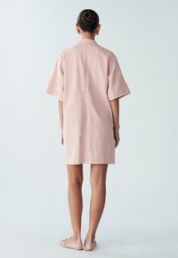 Krótka różowa sukienka z miękkiego, lekkiego materiału. Charakteryzuje się luźnym krojem, krótkimi rękawami oraz tylną kieszenią. Minimalistyczny design z czystymi liniami.