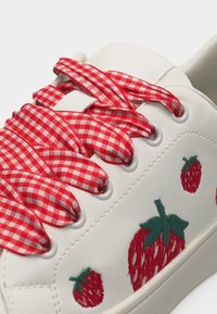 Baskets blanches avec des lacets à carreaux rouges et blancs et des fraises rouges brodées avec des feuilles vertes sur le côté.