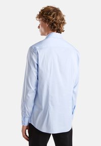 Camicia a maniche lunghe azzurro chiaro con una texture liscia, colletto a bottoni e orlo arrotondato; presenta polsini con bottoni e una vestibilità classica.