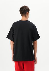 Sort T-shirt med løs pasform, korte ærmer og rund hals, lavet af blødt bomuldsstof. Bæres med røde træningsbukser.