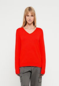 Κόκκινο πουλόβερ με V λαιμόκοψη, μακριά μανίκια, ριμπ μανσέτες και τελείωμα. Μαλακή υφή και άνετη εφαρμογή, συνδυασμένο με γκρι cargo παντελόνια.