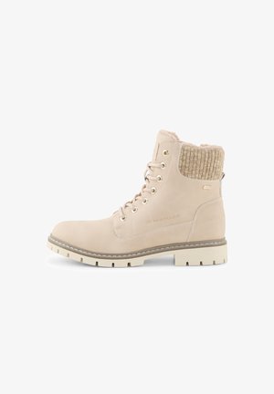 Botín de tobillo beige con cordones y puño de punto, punta redonda, suela gruesa y detalle de marca en el costado, diseñado para el uso invernal.