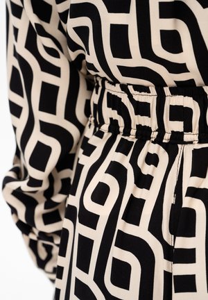 Czarny i beżowy materiał w geometryczny wzór z elastycznym pasem, prawdopodobnie część rękawa i talii ubrania.