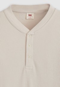 Beige ribbestripe henley-skjorte med rund krage, tre knapper og standard passform. Teksturt stoff med subtil detaljering.