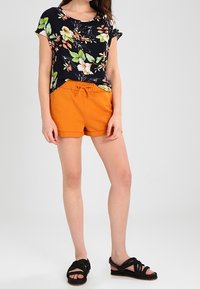 Halenka s květinovým potiskem, krátký rukáv v námořnické modré a zelené, doplněná oranžovými kraťasy na stažení a černými sandály na řemínky. Hladká tkanina a volný střih.