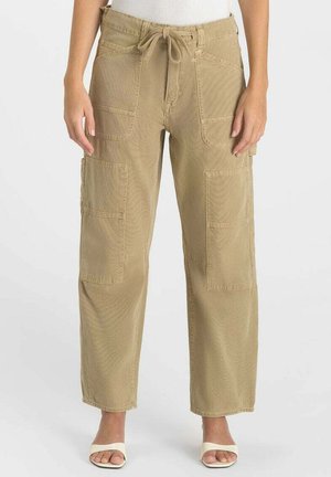 Vrouw draagt beige cargobroek met trekkoord in de taille en meerdere opgestikte zakken, gecombineerd met witte sandalen met hak.