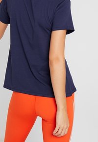 Navy blue, short-sleeved T-shirt made of soft fabric, paired with vibrant orange leggings featuring white side stripes.
