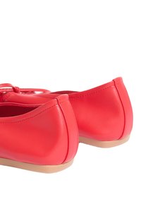 Ballerine rosse in pelle con texture liscia, punta arrotondata e suola in gomma beige bassa. Presentano un dettaglio con lacci sulla parte anteriore.