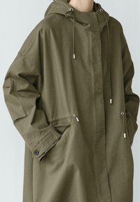 Olivgrüne, leichte Kapuzenparka mit Kordelzug, Seitentaschen und Knopfmanschetten. Glatter Stoff mit entspanntem Schnitt.